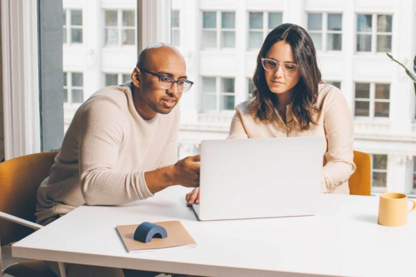 Duas pessoas, um homem e uma mulher, olhando para a tela de um computador enquanto conversam.